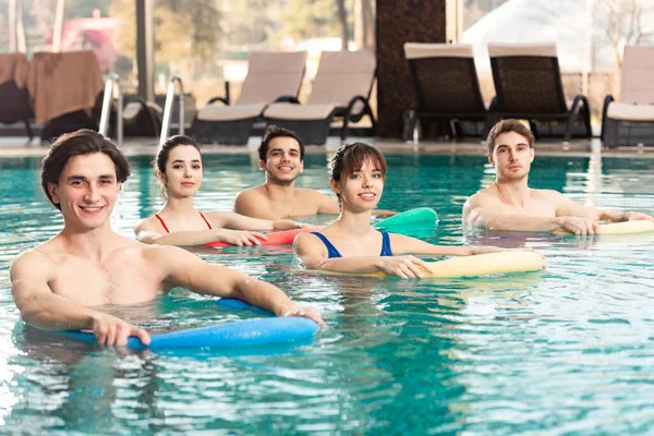 Группа молодых людей держала в бассейне лапшу для бассейна во время тренировки по водной гимнастике — стоковое фото
