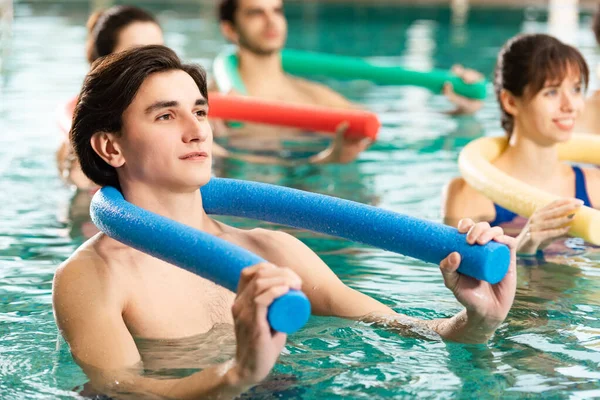 Foco seletivo do jovem homem segurando macarrão da piscina durante o exercício na piscina — Fotografia de Stock