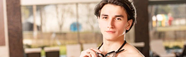 Panoramic shot of handsome man holding swimming googles and looking at camera — Stock Photo