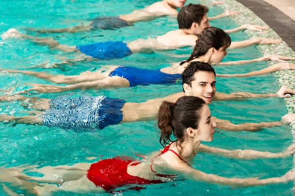Vista lateral de los jóvenes sonrientes ejercitando aeróbic acuático en la piscina - foto de stock