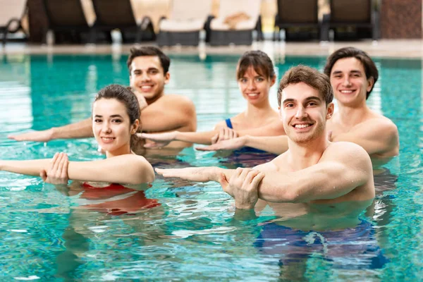 Выборочный фокус молодых людей, улыбающихся в камеру во время водной аэробики в бассейне — стоковое фото