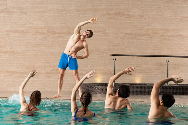 Allenatore sorridente che mostra esercizio al gruppo di persone in piscina — Foto stock