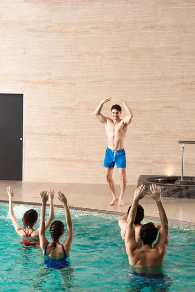 Guapo entrenador mostrando ejercicio a grupo de jóvenes entrenando en la piscina - foto de stock