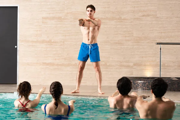 Selektiver Fokus eines gut aussehenden Trainers, der Wassergymnastik mit einer Gruppe von Menschen im Schwimmbad übt — Stockfoto