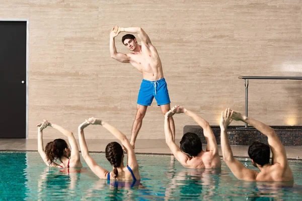 Guapo entrenador mostrando ejercicio a grupo de personas en la piscina durante aeróbic acuático - foto de stock