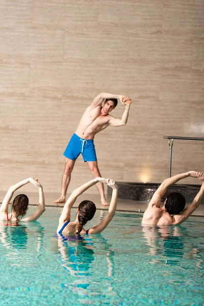 Красивий тренер тренувальної групи молодих людей у басейні під час водної аеробіки — стокове фото