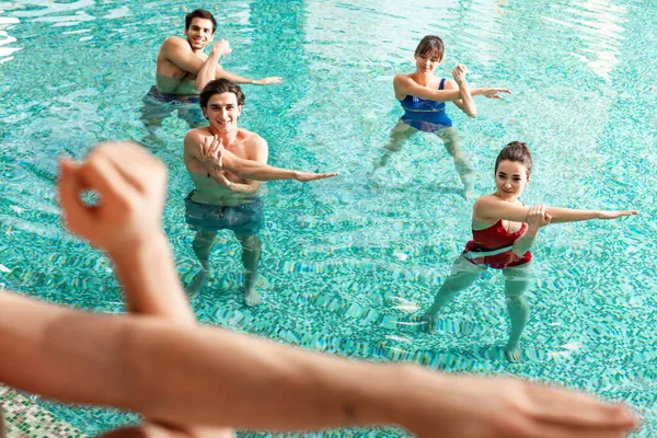 Focus selettivo delle persone sorridenti che guardano l'allenatore durante l'aerobica in piscina — Foto stock