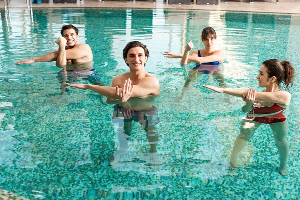 Группа улыбающихся молодых людей вместе тренируется в бассейне — стоковое фото