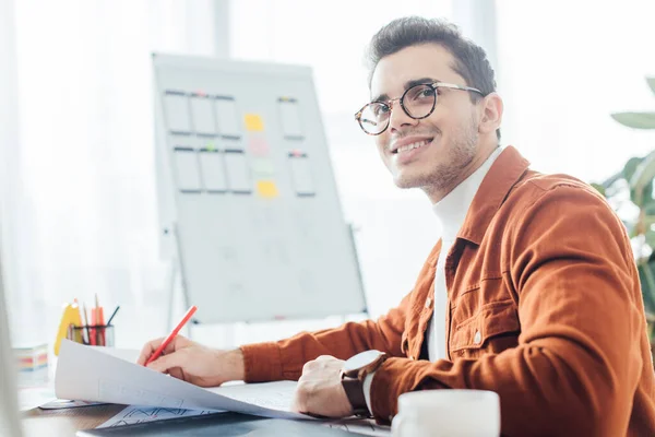 Side view of smiling ux designer holding marker while working with website templates at table — Stock Photo