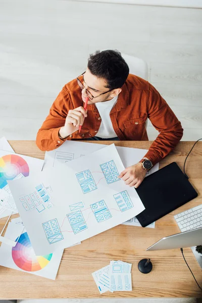 Visão geral do designer pensativo trabalhando com modelos de design de experiência do usuário na mesa — Fotografia de Stock