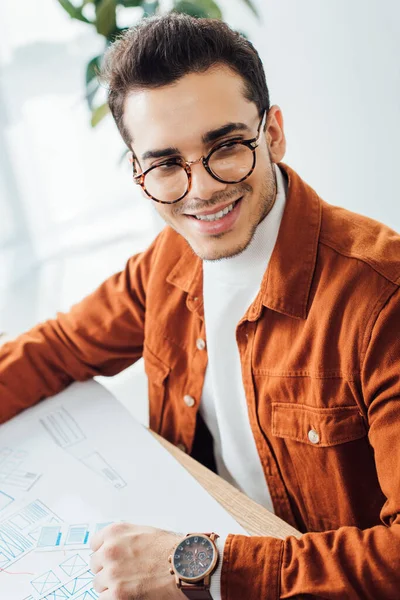 Développeur souriant regardant loin tout en planifiant la conception de l'expérience utilisateur à table dans le bureau — Photo de stock