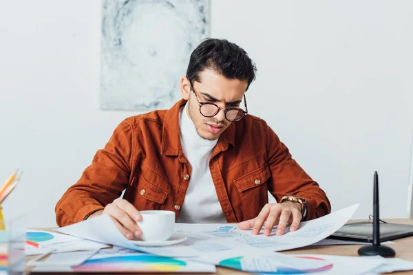 Diseñador Ux beber café mientras trabaja con plantillas de aplicaciones y círculos de color en la mesa - foto de stock