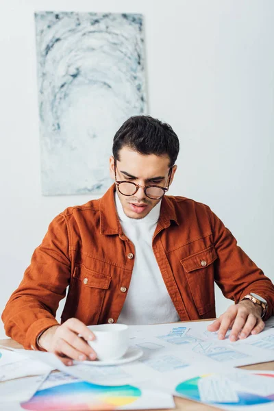 Selective focus of developer planning user experience design of website with layouts near coffee on table — Stock Photo