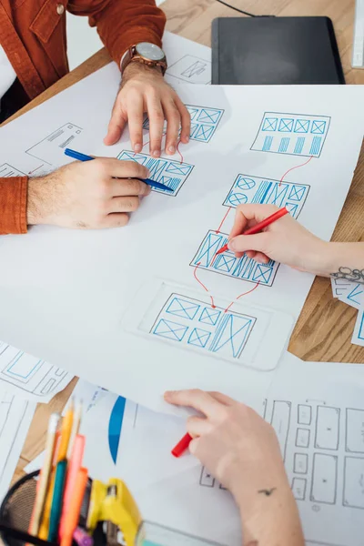 Ausgeschnittene Ansicht von UX-Designern, die mit Layouts und Skizzen auf dem Tisch arbeiten — Stockfoto