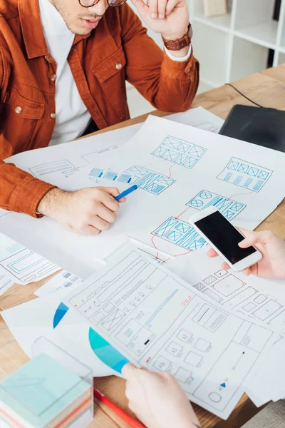 Ausgeschnittene Ansicht von UX-Designern mit Smartphone und Planungs-App-Frameworks für mobile Website am Tisch — Stockfoto