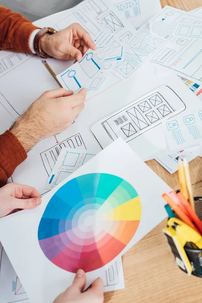 Ausgeschnittene Ansicht von Designern, die mit Vorlagen für UX-Design und Farbkreis auf dem Tisch arbeiten — Stockfoto