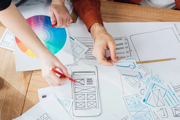 Zugeschnittene Ansicht von Designern, die User Experience Design mit Layouts und Farbkreis auf dem Tisch planen — Stockfoto