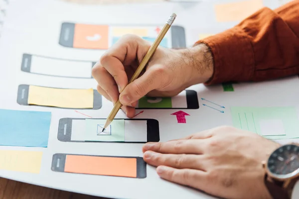 Cropped view of developer noticing on app layouts for user experience design of mobile website on table — Stock Photo