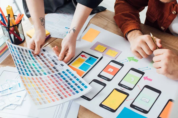 Vista recortada de diseñadores que planean el diseño de la experiencia del usuario con paleta de colores y bocetos del sitio web en la mesa — Stock Photo