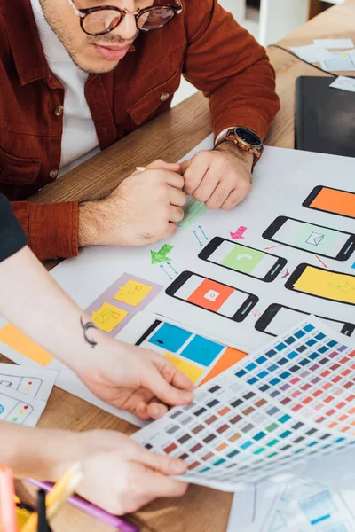 Vista recortada de diseñadores con diseño de experiencia de usuario de planificación de paleta de colores en la mesa - foto de stock