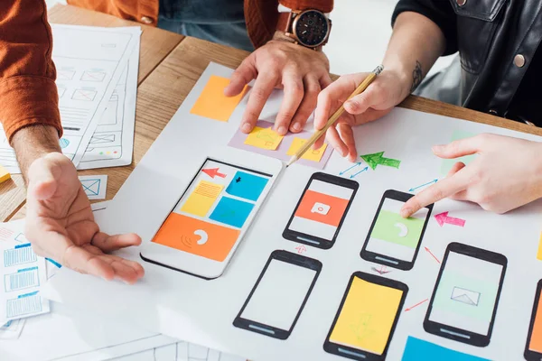 Cropped view of developers creative user experience design of mobile website with layouts on table isolated on grey — Stock Photo