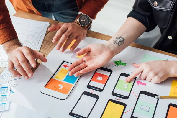 Vista recortada de los diseñadores de ux que trabajan con bocetos y diseños de marcos de cables móviles en la mesa - foto de stock