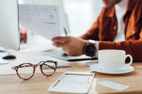 Selective focus of eyeglasses and layouts of ux design near designer working at table — Stock Photo