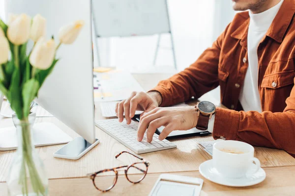 Vista recortada del desarrollador utilizando el ordenador cerca de plantillas de diseño ux y café en la mesa - foto de stock