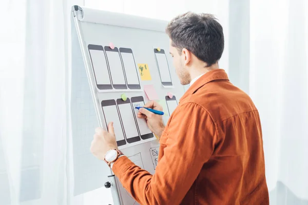 Vue latérale du concepteur créatif en utilisant des cadres mobiles tout en développant la conception de l'expérience utilisateur du site Web sur tableau blanc — Stock Photo