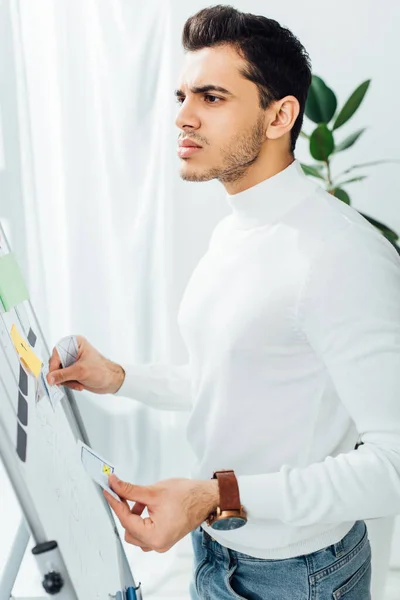 Vue latérale du développeur ux onéreux tenant des mises en page d'applications près du tableau blanc dans le bureau — Photo de stock