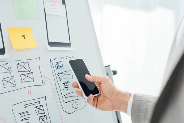 Selective focus of ux designer using smartphone near sketches and layouts on whiteboard in office — Stock Photo