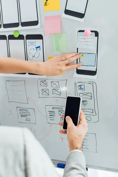 Ausgeschnittene Ansicht von UX-Designern mit Smartphone und Skizzen der App-Oberfläche auf Whiteboard im Büro — Stockfoto