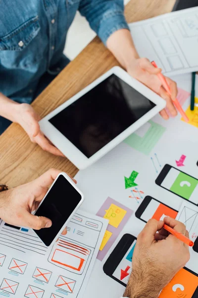 Enfoque selectivo de los diseñadores ux utilizando teléfonos inteligentes y tabletas digitales cerca de los marcos móviles en la mesa aislados en gris - foto de stock