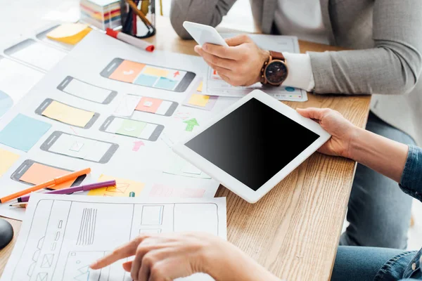 Vista recortada de los diseñadores ux utilizando gadgets cerca de los marcos móviles en la mesa aislado en gris - foto de stock