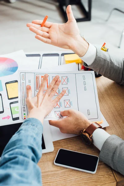 Vista recortada de los diseñadores ux que trabajan con plantillas de sitio web cerca de los marcos y gadgets en la mesa - foto de stock