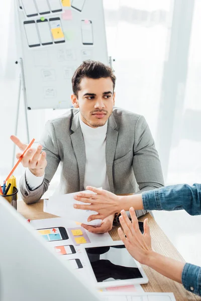 Selective focus of designer showing stop gesture to colleague near layouts of user experience design on table — Stock Photo