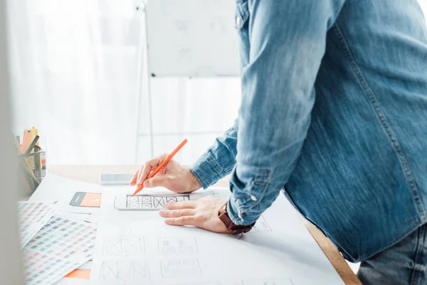 Vista recortada del diseñador ux que trabaja con bocetos de interfaz móvil y paletas de colores en la mesa - foto de stock