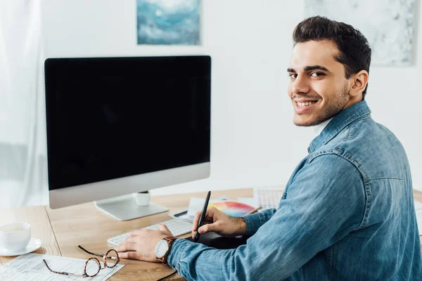 Designer lächelt in die Kamera, während er an einem User Experience Design-Projekt in der Nähe von Computer und Grafik-Tablet auf dem Tisch arbeitet — Stockfoto
