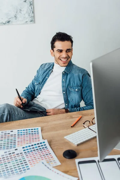 Sorrindo ux designer usando gráficos tablet e computador perto de paletas de cores na mesa — Fotografia de Stock