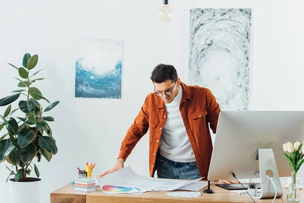 Schöner UX-Designer arbeitet mit Farbkreisen und Website-Skizzen in der Nähe des Computers auf dem Tisch — Stockfoto