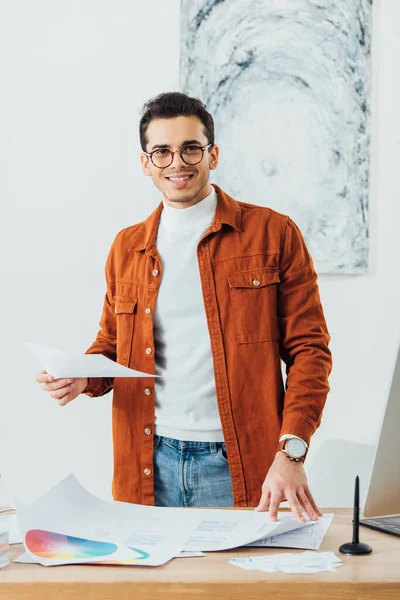Designer Ux sorride alla fotocamera mentre lavora con cerchi di colori e modelli di user experience design a tavola — Foto stock