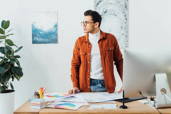 Diseñador mirando hacia otro lado cerca de gadgets, círculos de color y diseños de diseño de experiencia de usuario en la mesa - foto de stock