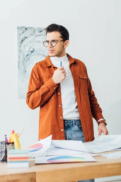 Selective focus of thoughtful designer holding marker near color circles and sketches of website design on table — Stock Photo