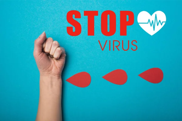 Top view of paper drops of blood near female fist on blue background, stop virus illustration — Stock Photo