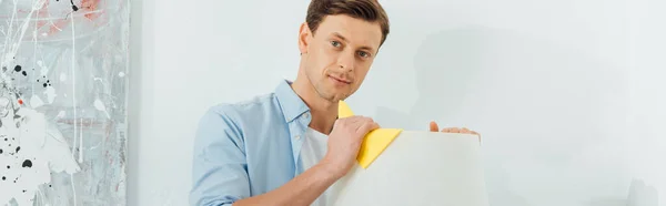 Handsome man looking at camera while cleaning floor lamp with rag, panoramic shot — Stock Photo