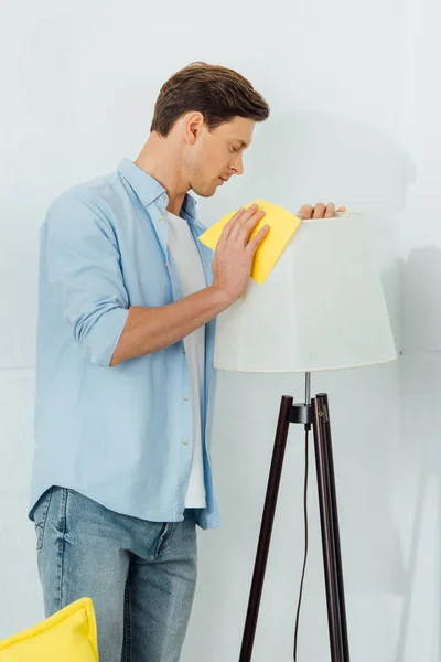 Vue latérale de l'homme nettoyage lampadaire avec chiffon dans le salon — Photo de stock