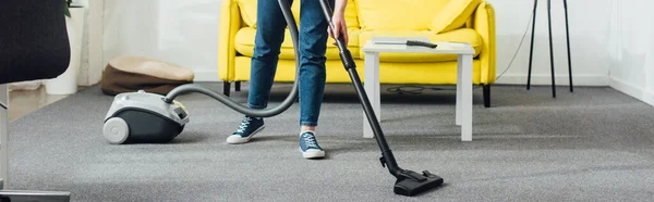 Vista cortada de mulher tapete de limpeza com aspirador de pó na sala de estar, tiro panorâmico — Fotografia de Stock