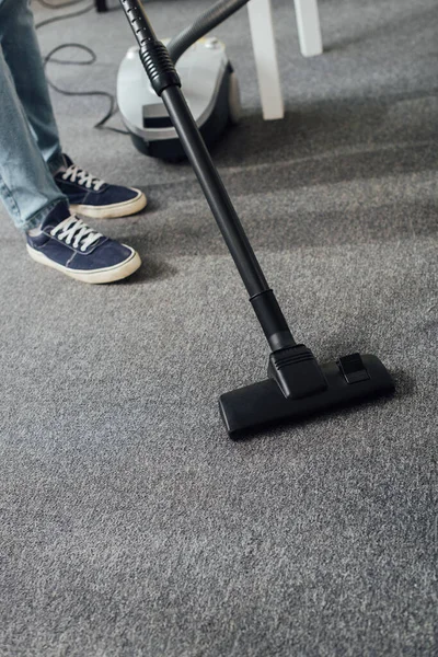 Обрізаний вид людини, що прибирає килим у вітальні з пилососом — стокове фото