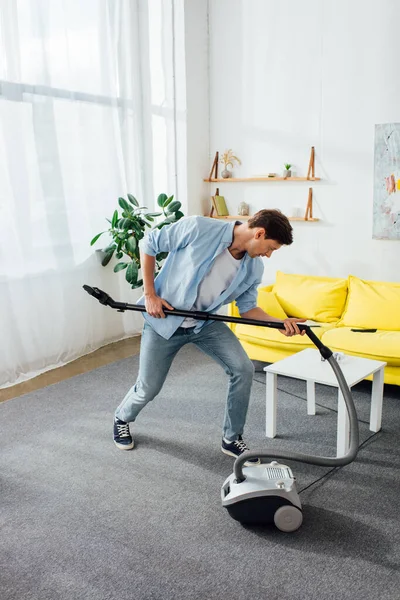 Чоловік тримає щітку пилососа під час прибирання у вітальні — стокове фото