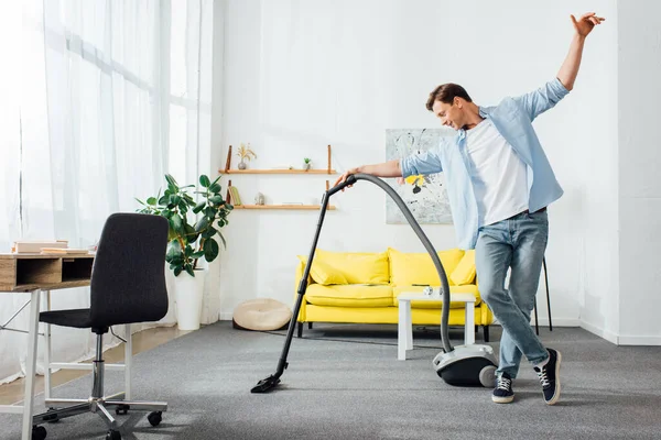 Bel homme nettoyage tapis avec aspirateur dans le salon — Photo de stock